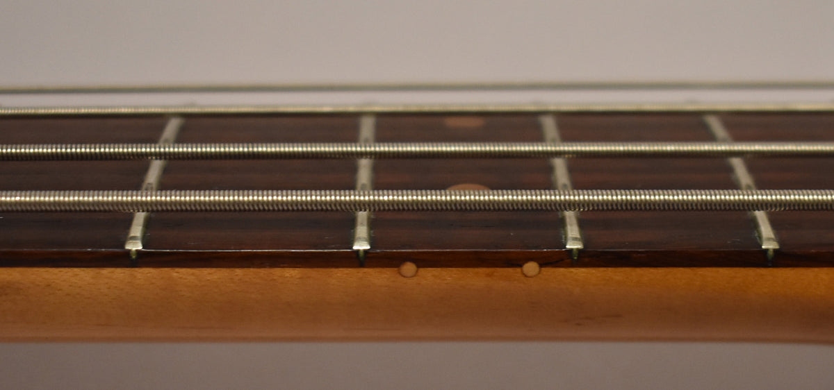 Close-up of the bass's dark rosewood fretboard and light maple neck, showing four frets, four strings, and two side dots.