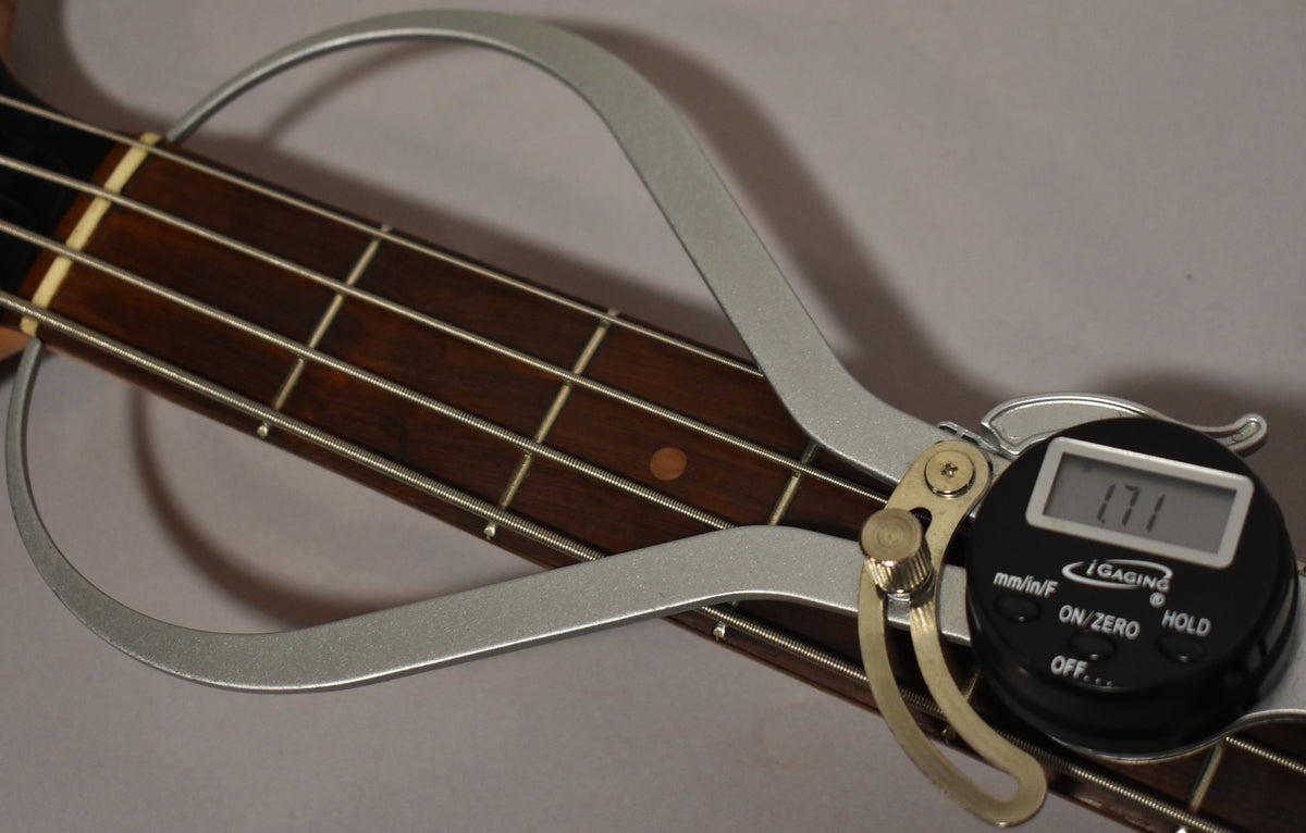 A digital caliper measures the dark rosewood fretboard of the bass, showing a reading of 1.71.