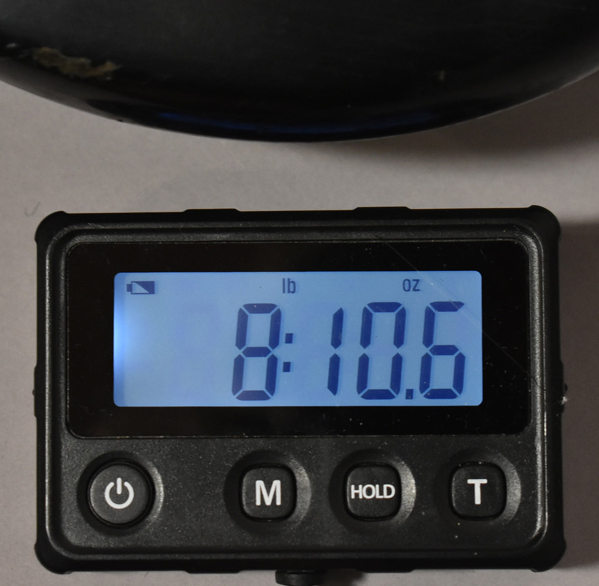 A digital scale displays "8:10.6" in pounds and ounces, with a black bass body partially visible above.