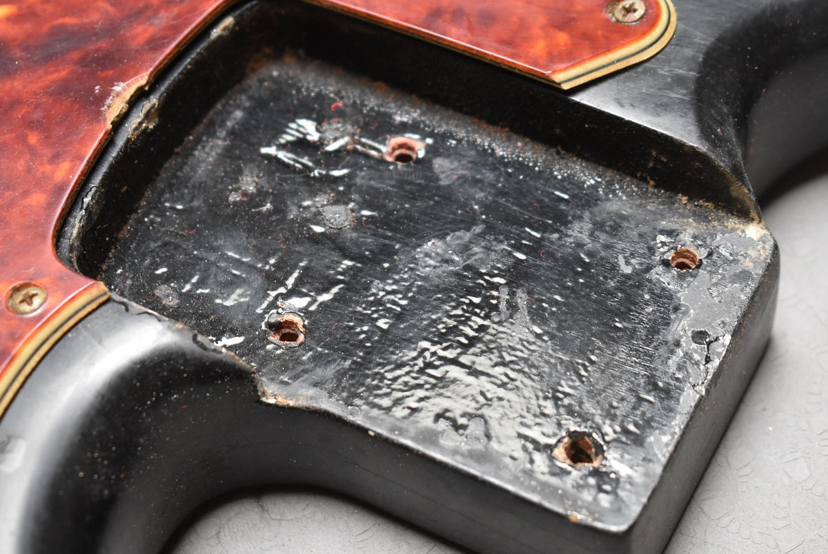 Close-up of the black body's control cavity, showing chipped paint, exposed wood, and four screw holes.