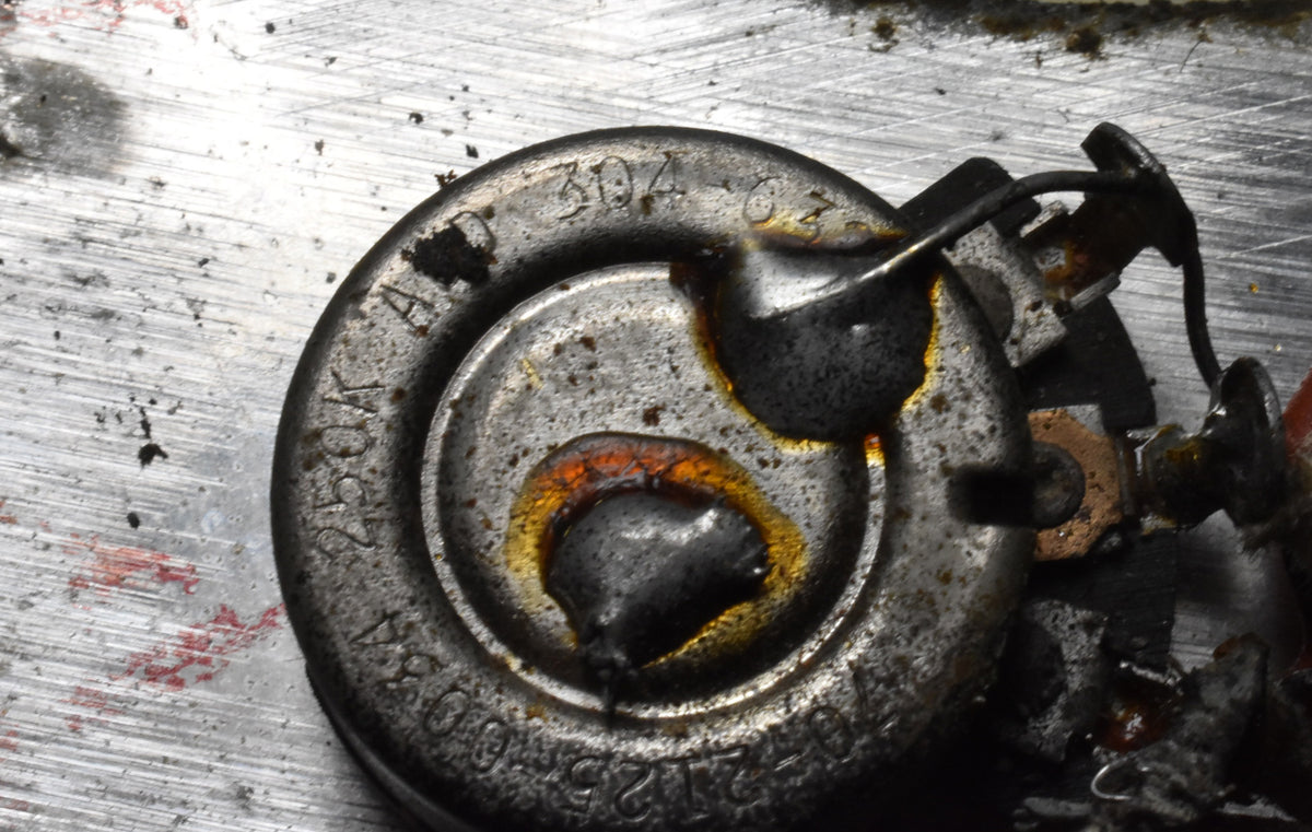 Close-up of a corroded metal potentiometer with solder residue and wires, showing stamped numbers and a rusty finish.