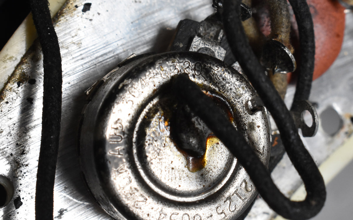 Close-up of a tarnished metal potentiometer with visible solder, wired with black cloth-covered wire and a red capacitor.