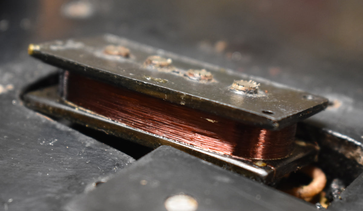 Close-up of the bass pickup, showing copper wire coils, rusted pole pieces, and a worn black cover.