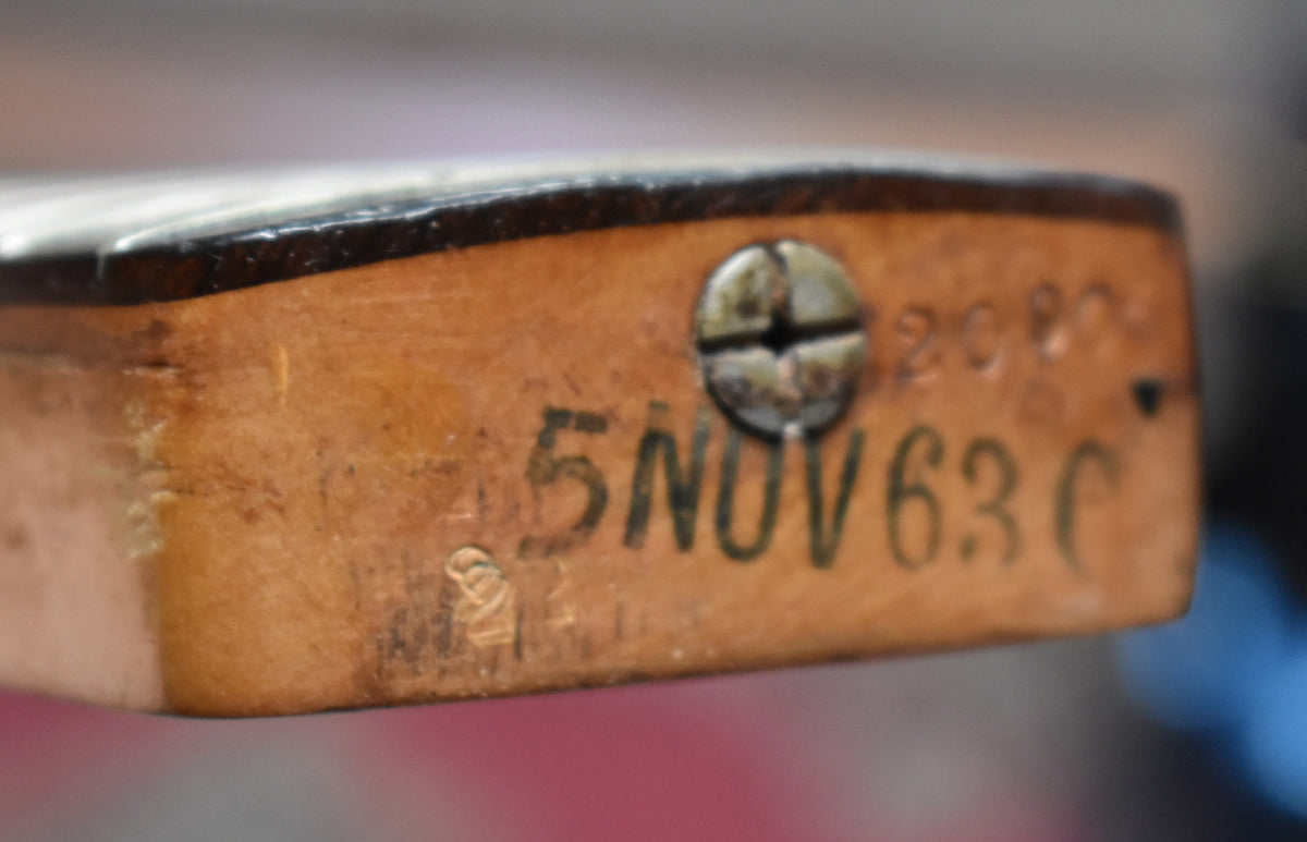 Close-up of the neck heel, showing a dark finish edge, a rusty screw, and "5 NOV 63 C" stamped into the worn wood.