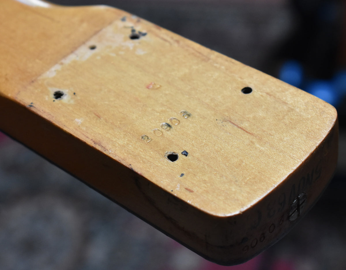 Close-up of the bass neck heel, showing four screw holes, a stamped serial number, and some pencil markings.