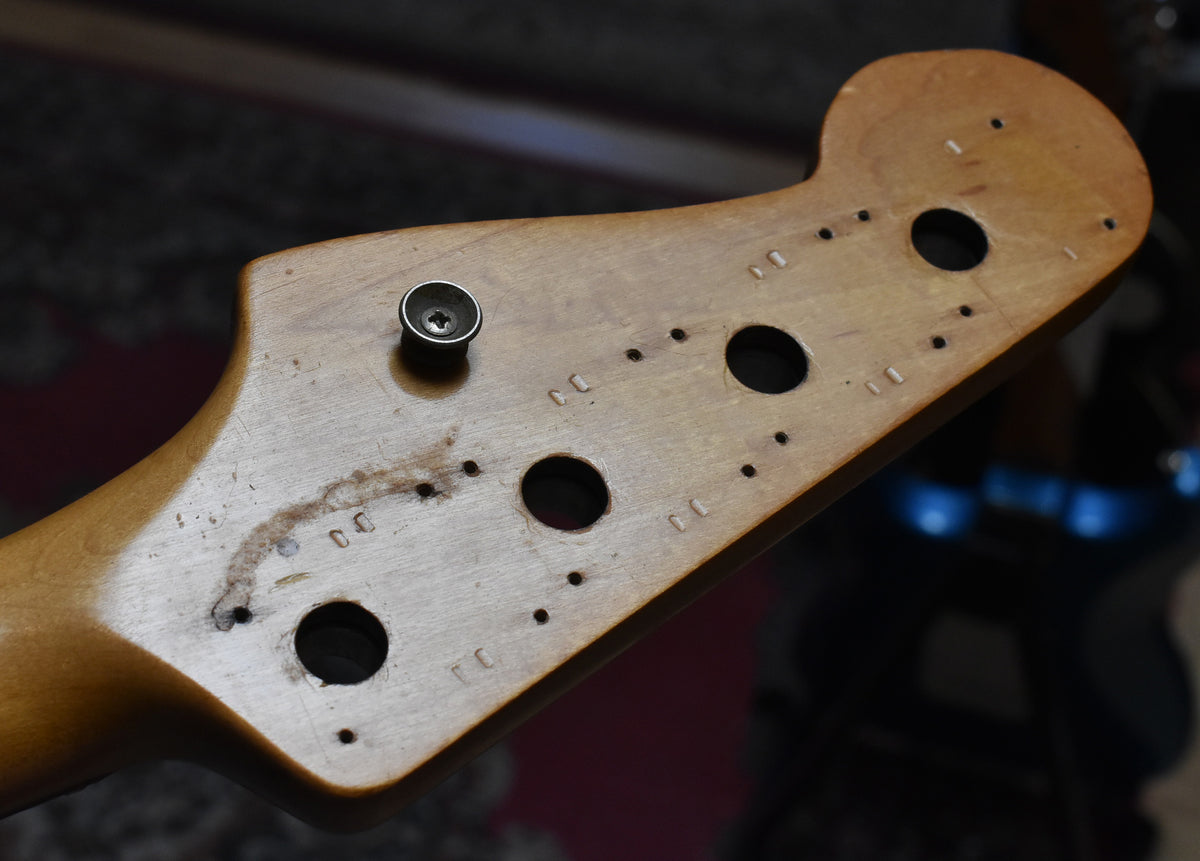 Close-up of the bass headstock's back, showing a single string tree, four tuner holes, and numerous screw holes from previous tuners.