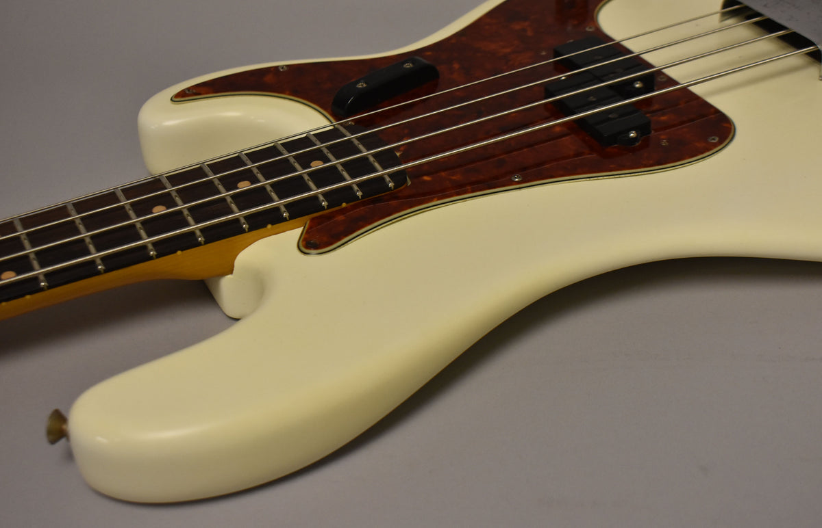 The Olympic White bass body, with a tortoiseshell pickguard and split-coil pickup, shows minor wear and a brass strap button.