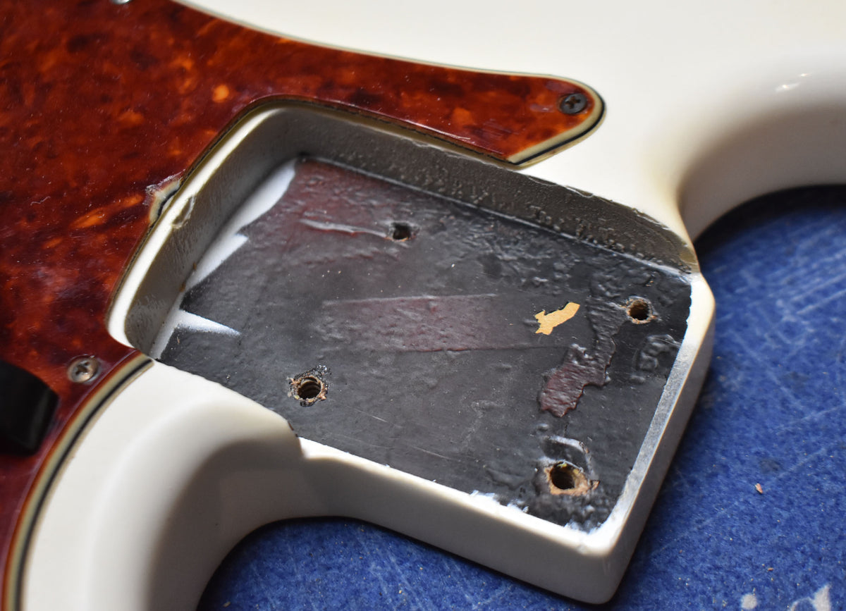 Close-up of the bass body's pickup cavity, showing the Olympic White finish, tortoiseshell pickguard, and black shielding paint.