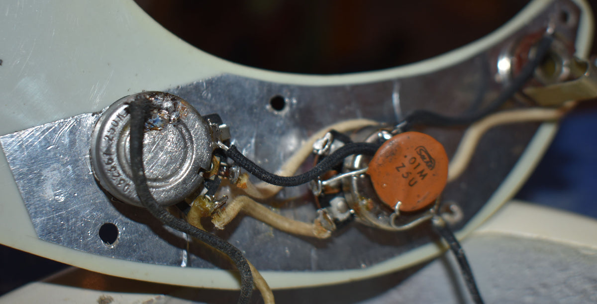 Close-up of the bass's control cavity, showing two pots, an orange capacitor, and vintage-style cloth wiring on a metal plate.