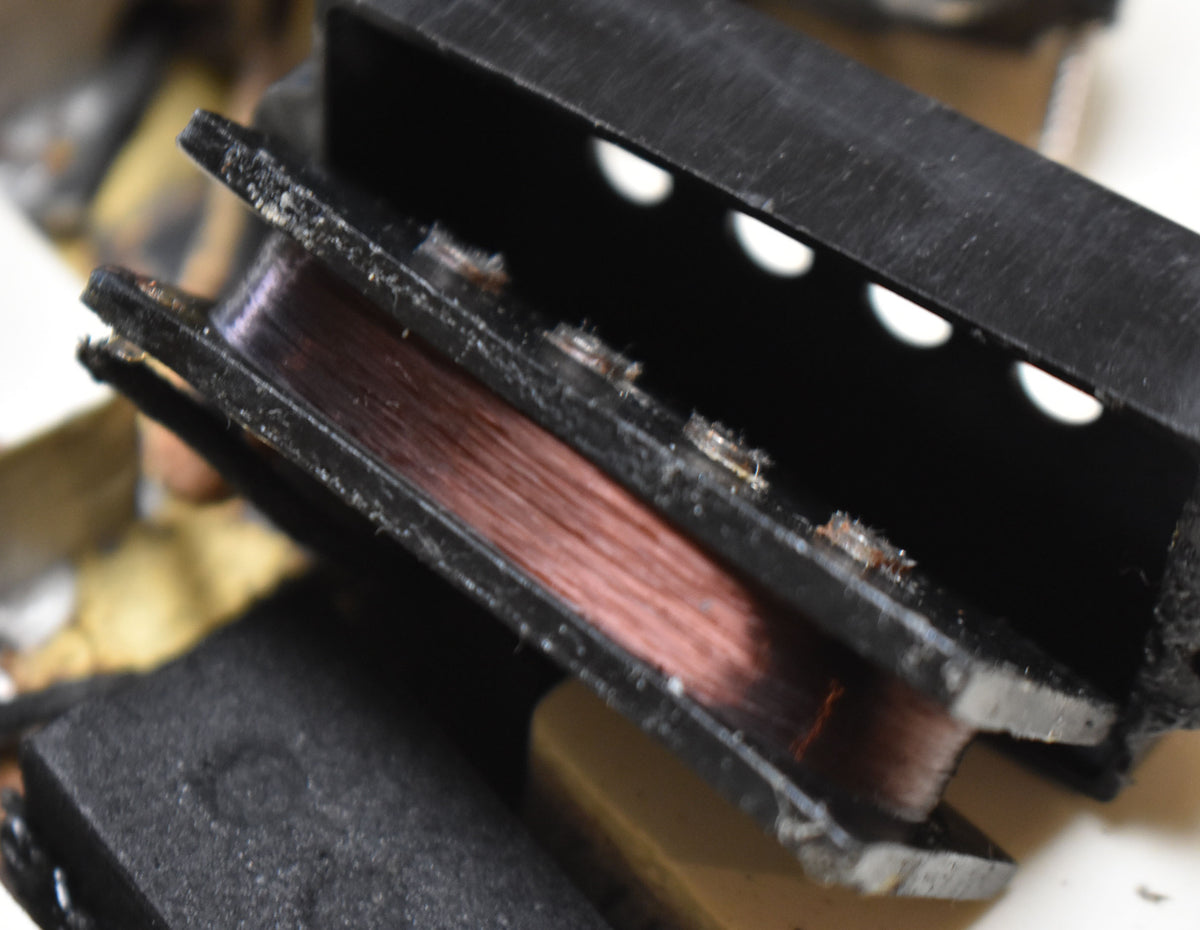 Extreme close-up of a pickup coil, showing copper wire wrapped around a black bobbin with visible dust and grime.