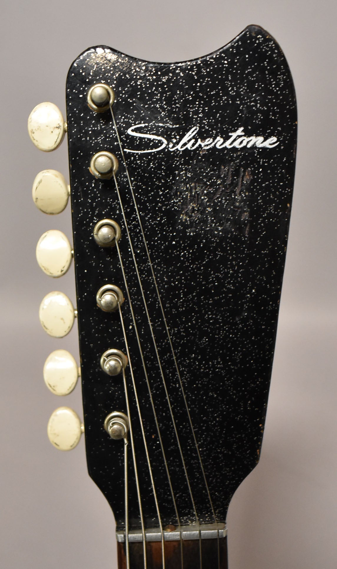 Close-up of the black, glitter-flecked headstock with six cream-colored tuning pegs and visible wear on the finish.