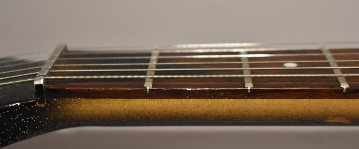 Close-up of the guitar's dark brown fretboard with metal frets and strings, showing a worn sunburst finish on the neck.