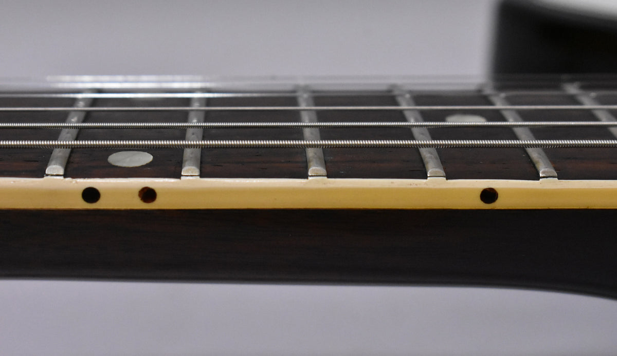 Close-up of the dark rosewood fretboard with cream binding, showing frets, strings, and a single mother-of-pearl dot inlay.