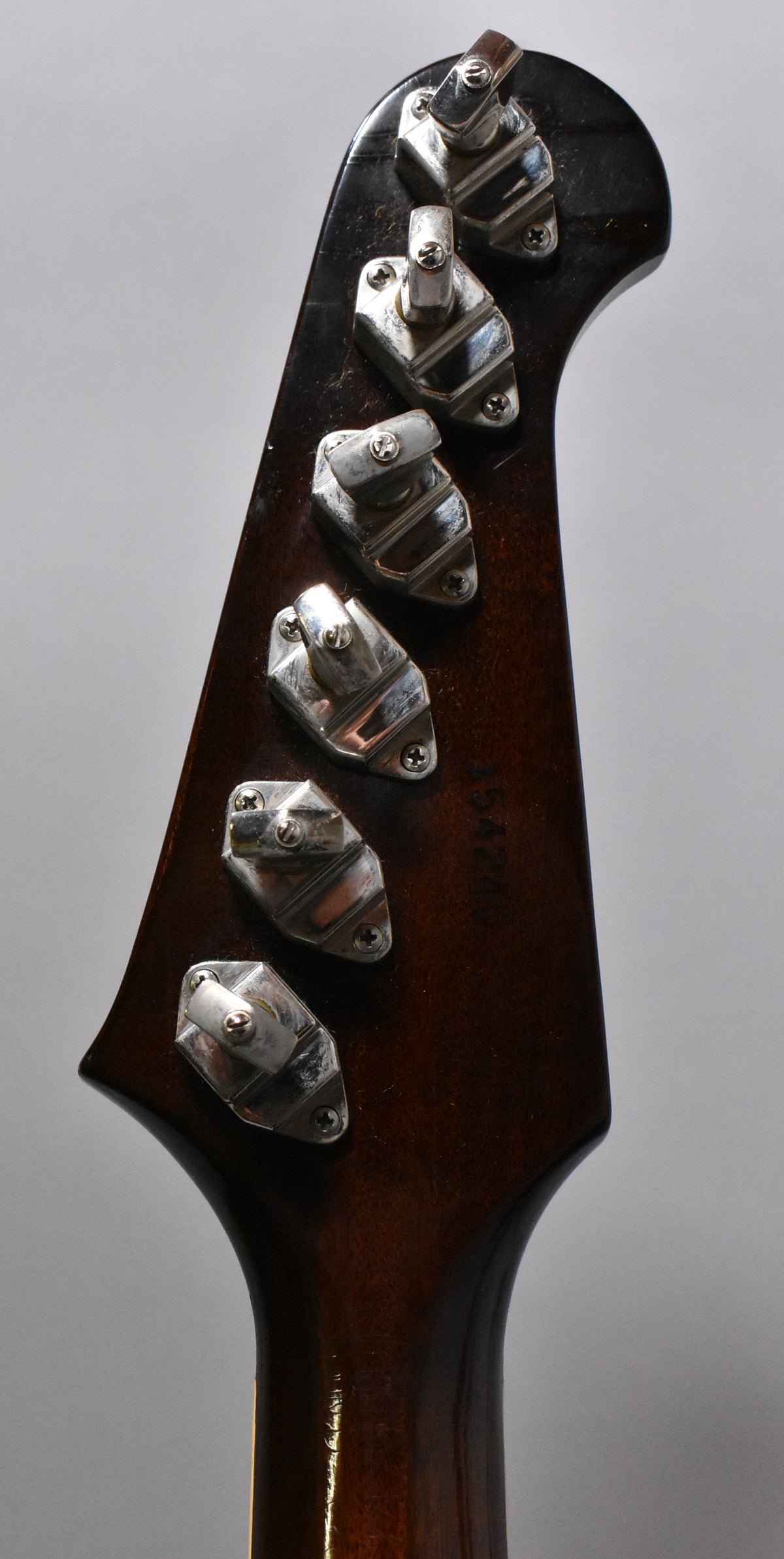 The back of a dark sunburst headstock and neck, showing six chrome tuners with visible wear and a faint serial number.