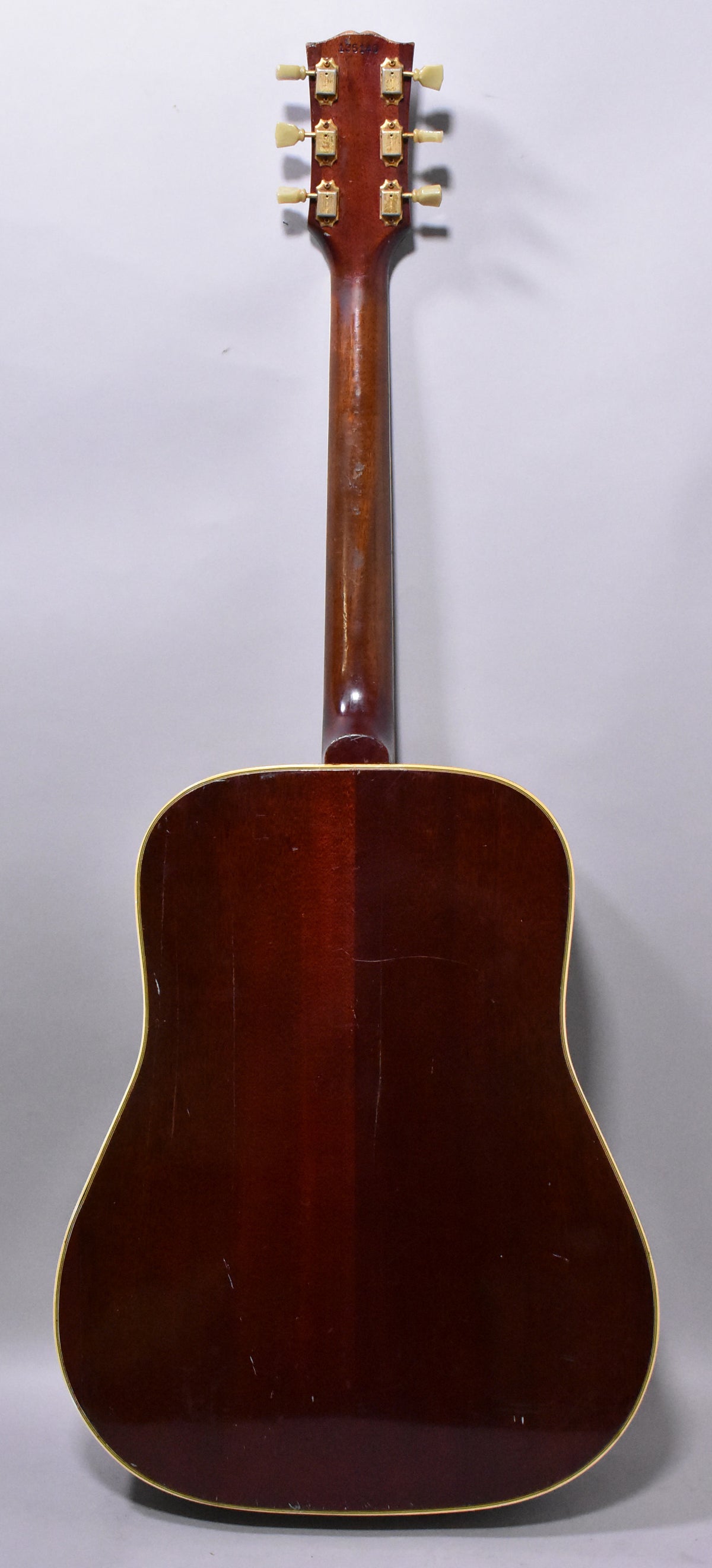 Full rear view of a dark sunburst acoustic guitar with light binding, showing finish checking and wear on the body and neck.