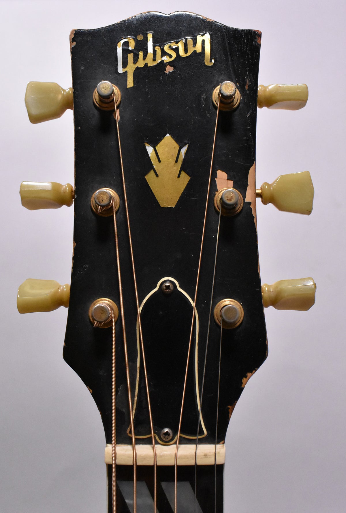 Close-up of the guitar's black headstock, showing gold tuning pegs with cream buttons and significant finish wear and chipping.
