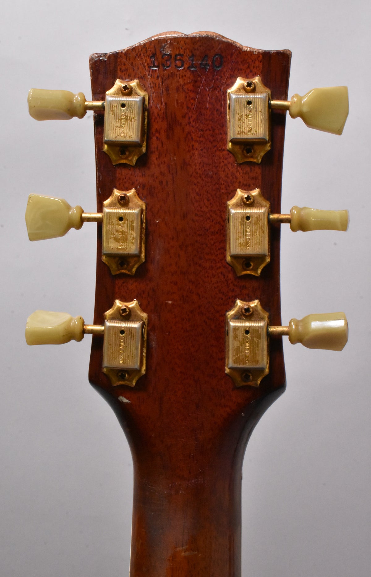 The back of the guitar's headstock, showing six gold-plated tuners with cream buttons, and a serial number stamped at the top.