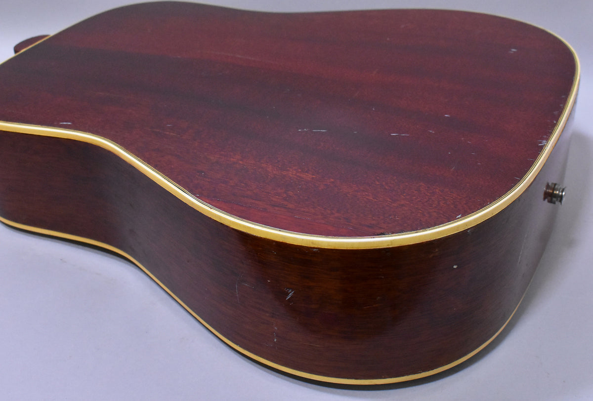 The guitar's dark reddish-brown back and side are visible, showing light scratches, wear, and cream binding.