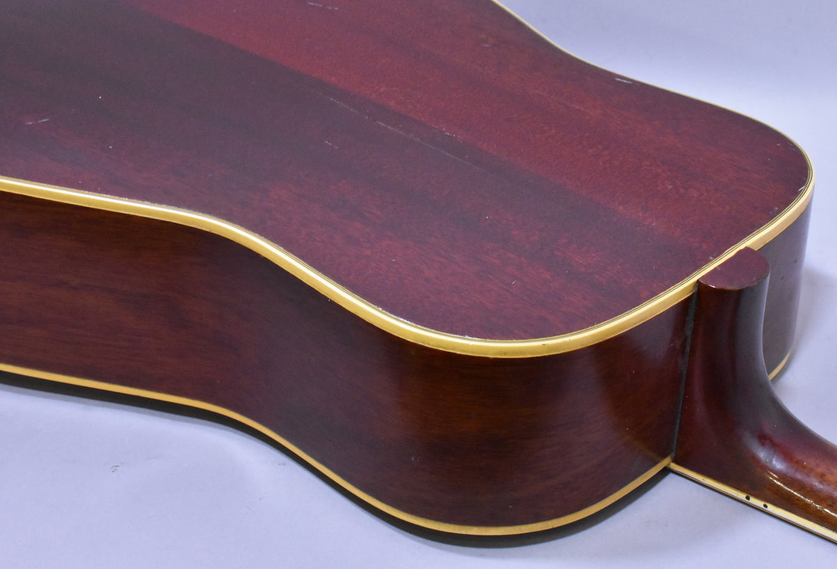 The guitar's dark cherry sunburst back and side are shown from the lower bout, with cream binding and light finish wear.