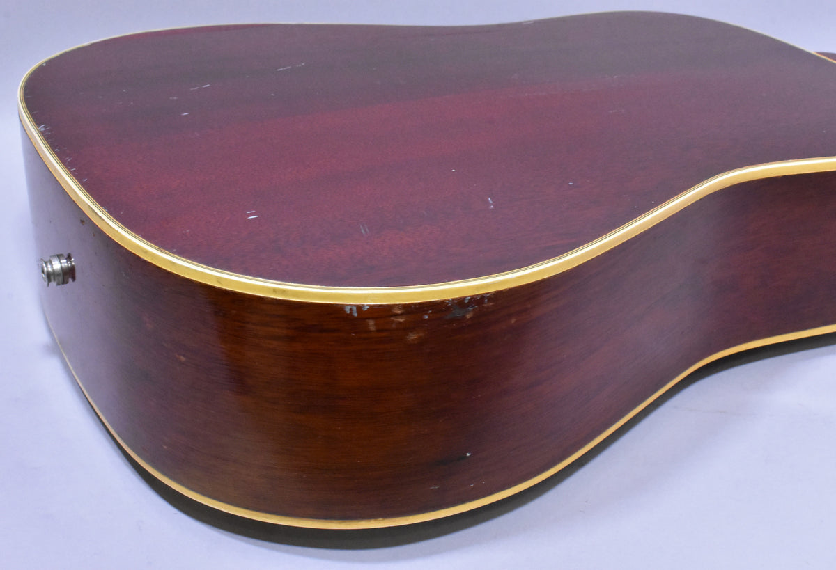 The lower bout of the sunburst acoustic guitar, showing the dark red back and brown sides with cream binding and visible finish wear.
