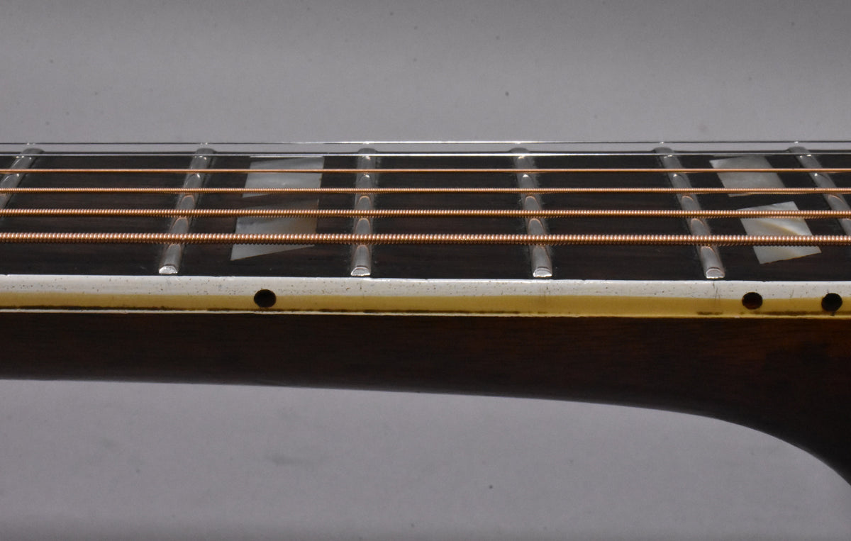 Close-up of the guitar's dark fretboard, showing copper strings, metal frets, trapezoid inlays, and side dots on the worn binding.