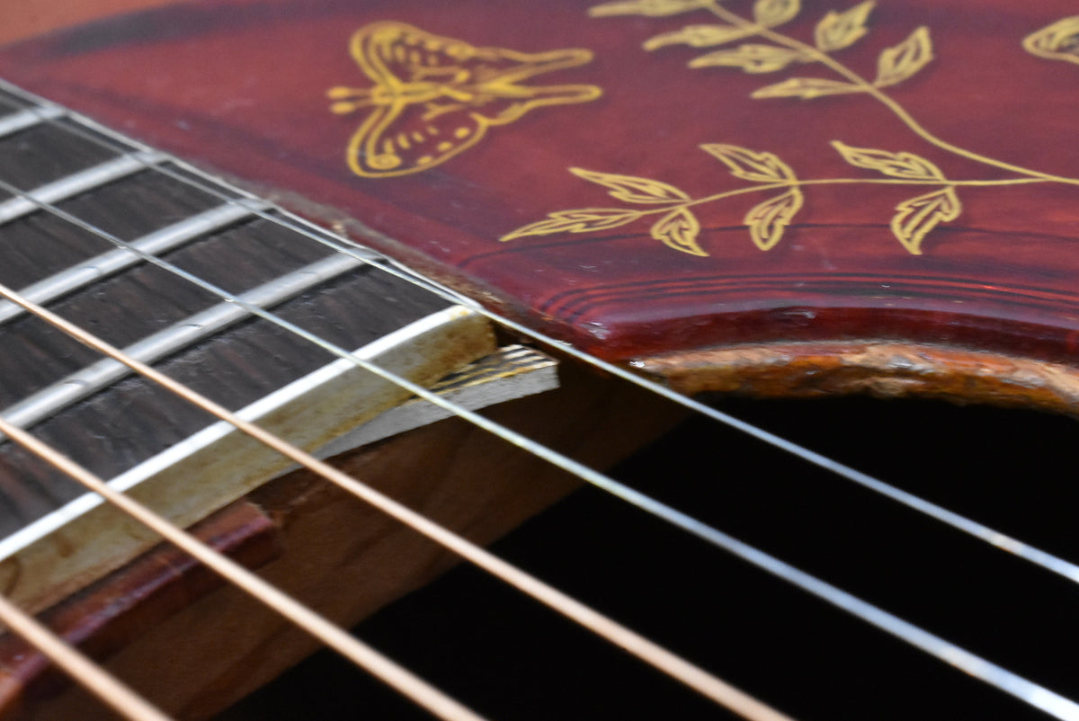 Close-up of the sunburst body and fretboard, showing the butterfly pickguard inlay, strings, and wear around the soundhole.