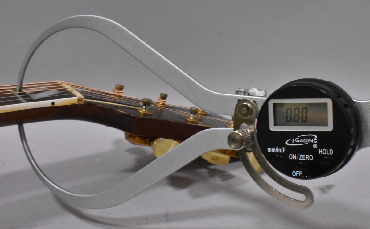 Close-up of the guitar's headstock and nut, with a digital caliper measuring the nut width, showing a reading of 0.00.