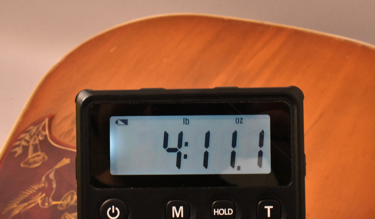 A digital scale displays "4:11 lb oz" over the sunburst finish of the guitar's body, showing some light wear and checking.