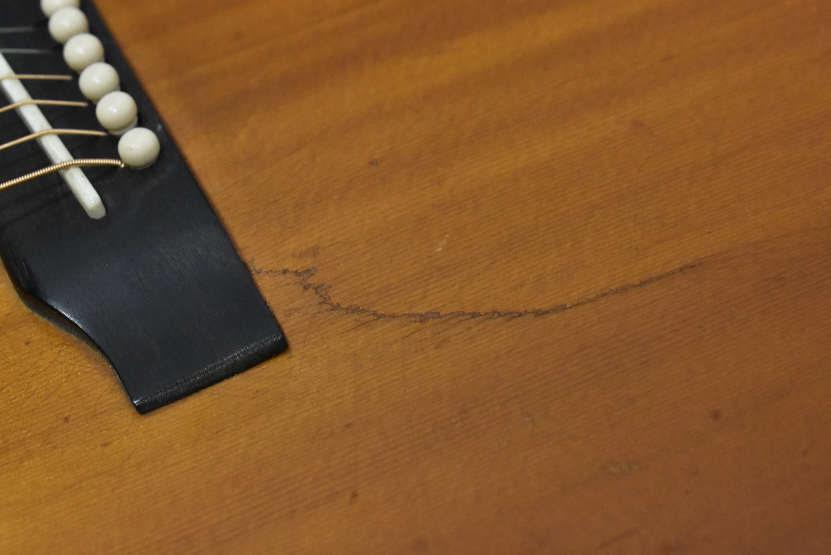 Close-up of the sunburst body, showing the black bridge with white pins and saddle, and a long, thin crack in the wood.