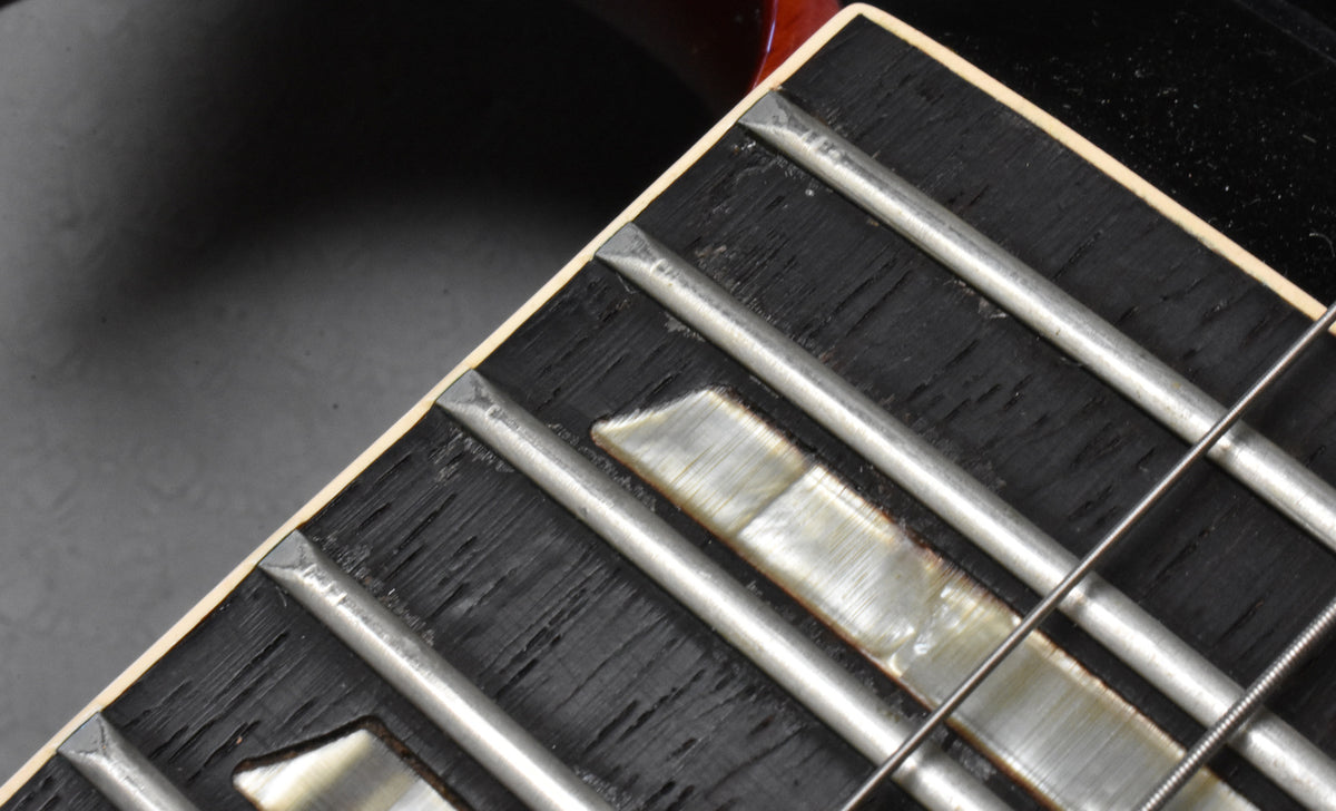 Close-up of the dark fretboard with rectangular mother-of-pearl inlays, showing wear and string grooves on the frets.