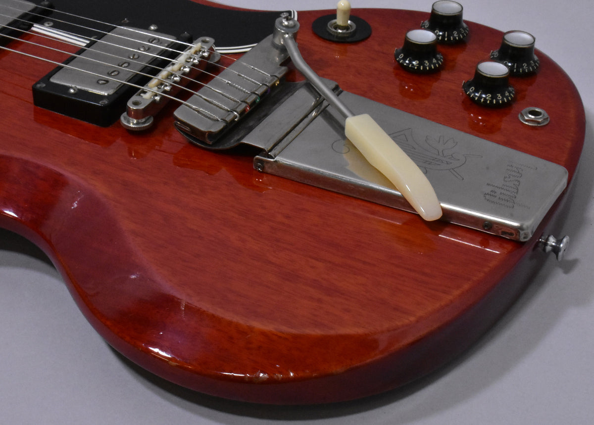 Close-up of the cherry red body, showing the bridge, vibrato tailpiece with cream arm, four black control knobs, and some finish wear.