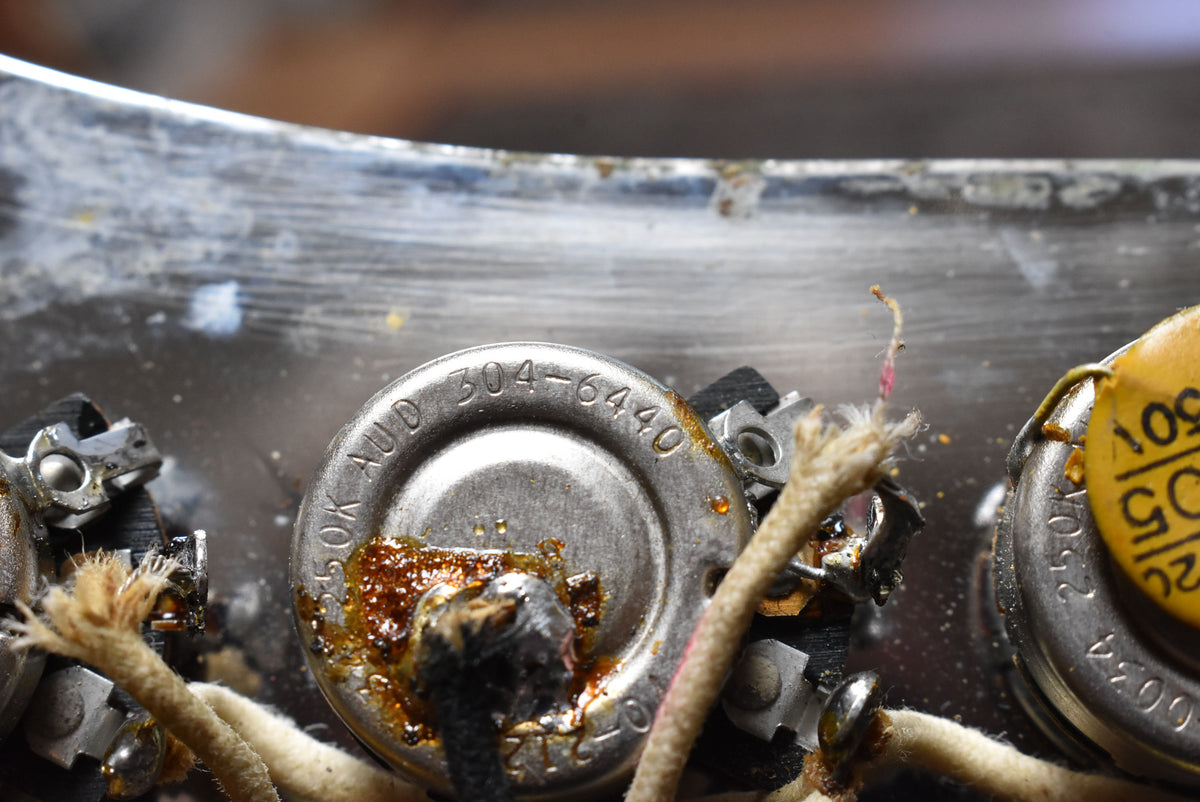 Close-up of the bass's internal wiring, showing a tarnished metal potentiometer with visible solder joints and cloth-covered wires.