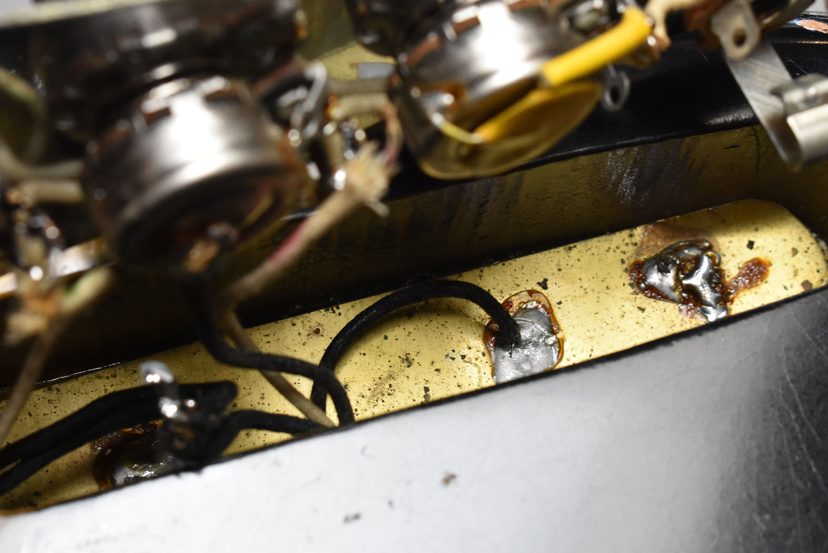 A close-up of the bass's internal wiring and pots, showing solder joints and a gold-colored cavity with some grime.