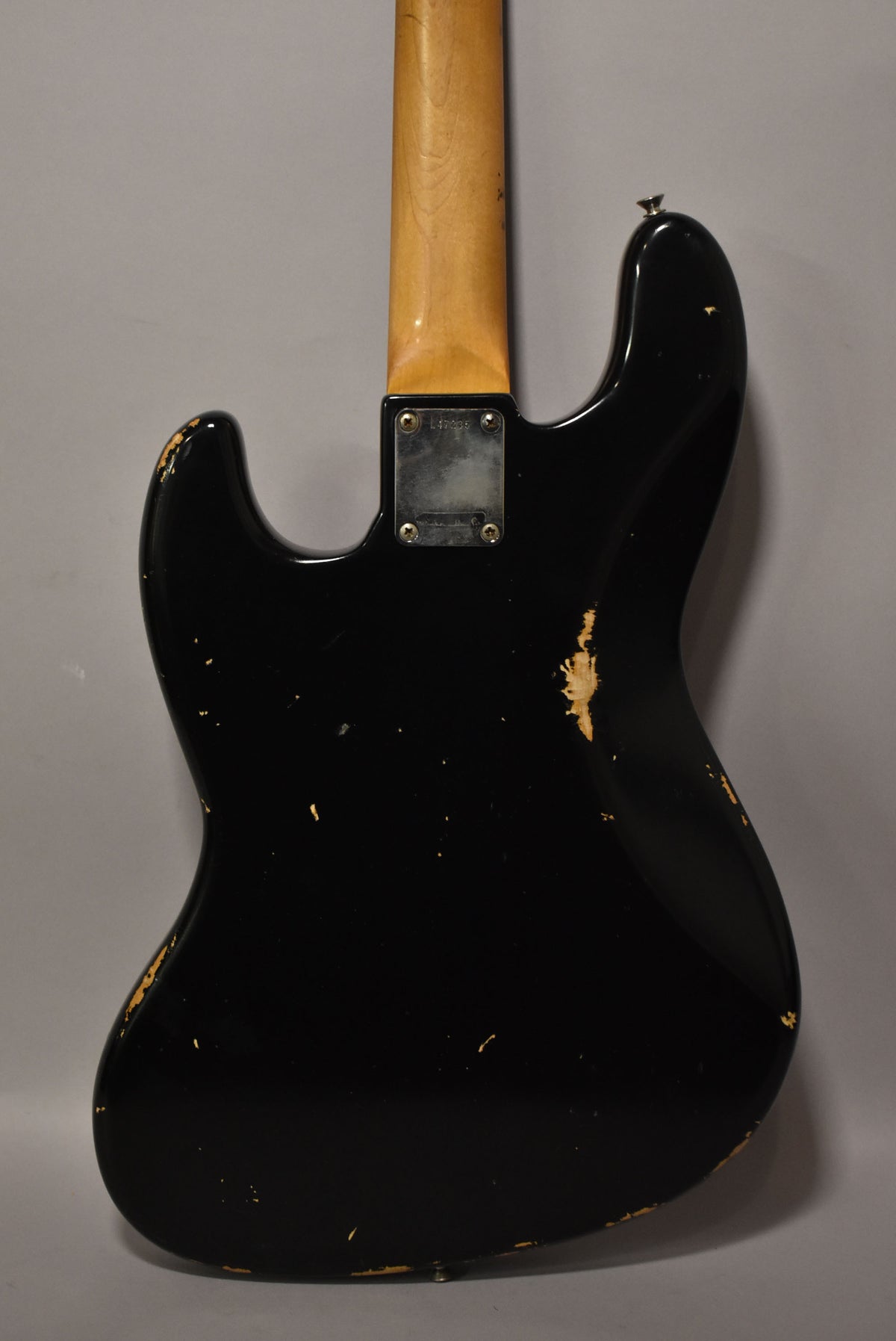 The black refinished bass guitar's back shows heavy wear, with large chips revealing the wood and many small nicks across the body.