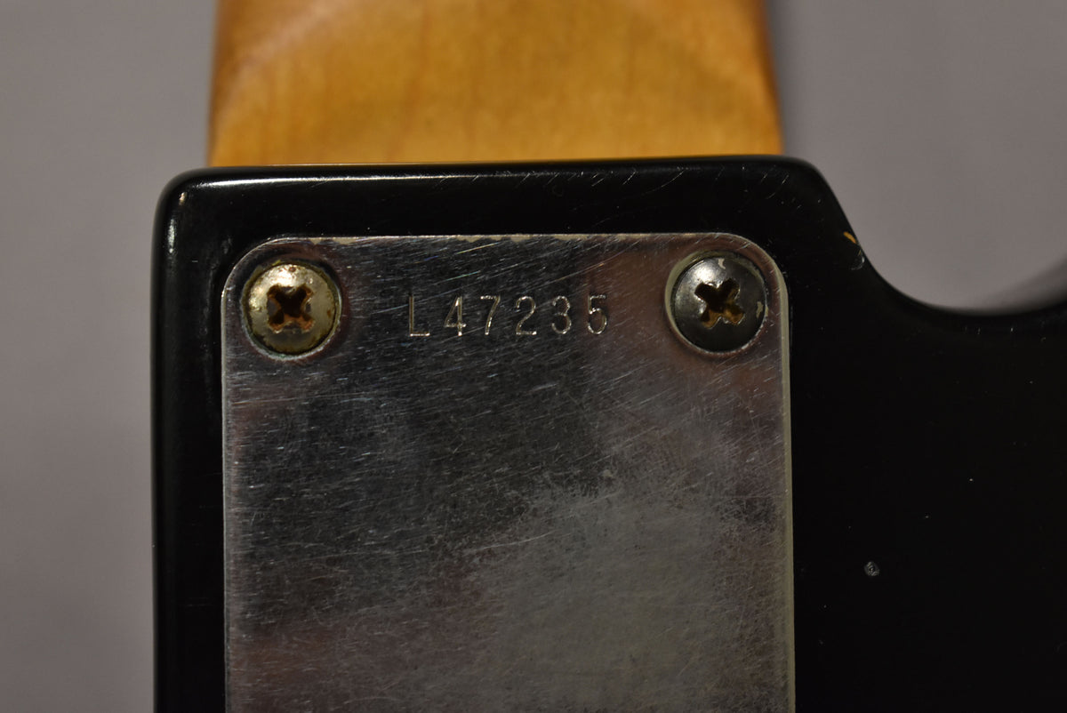 Close-up of the neck plate, showing the serial number L47235, two worn screws, and some finish wear on the black body.