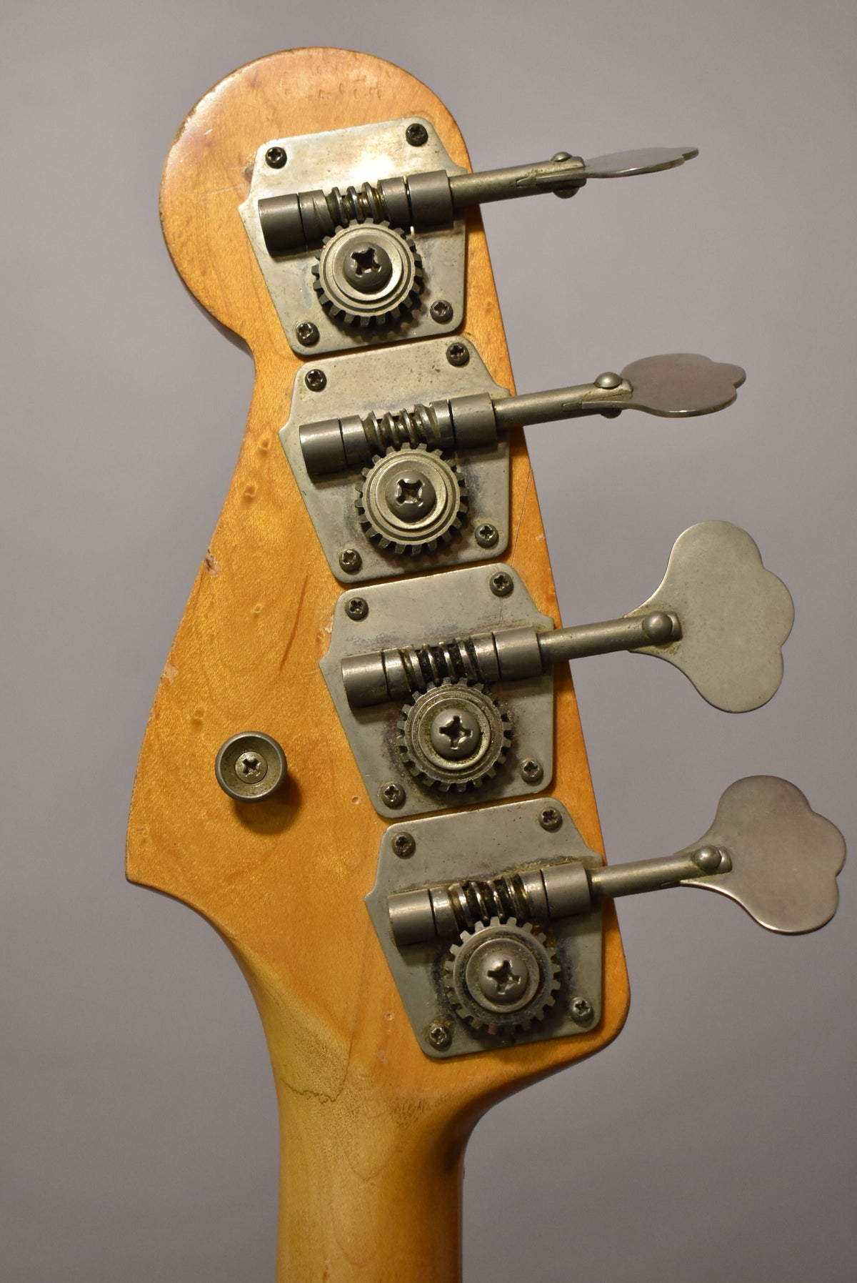Close-up of the bass headstock from behind, showing four worn, tarnished open-gear tuners with clover-leaf keys.