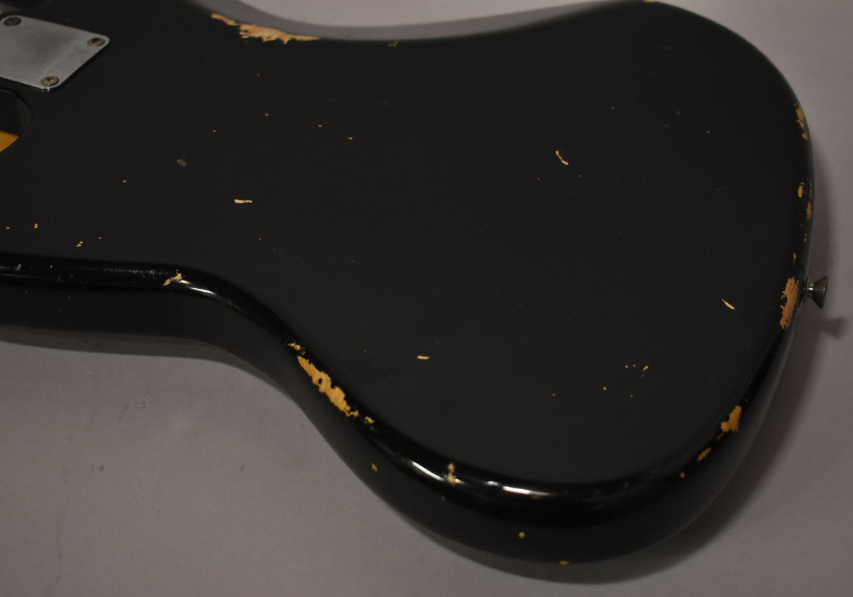 Close-up of the black refinished bass body, showing extensive paint chipping and wear along the edges and surface, revealing the wood beneath.