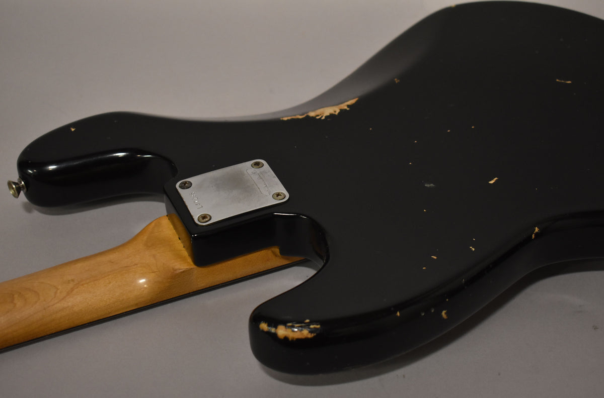 Rear view of a black refinished bass body with significant paint chips and wear, revealing lighter wood underneath.