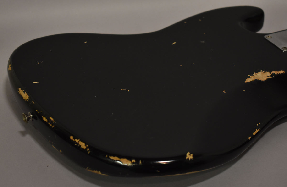 The black bass body, viewed from the back, shows significant paint chipping along the edges and a large worn patch near the upper horn.
