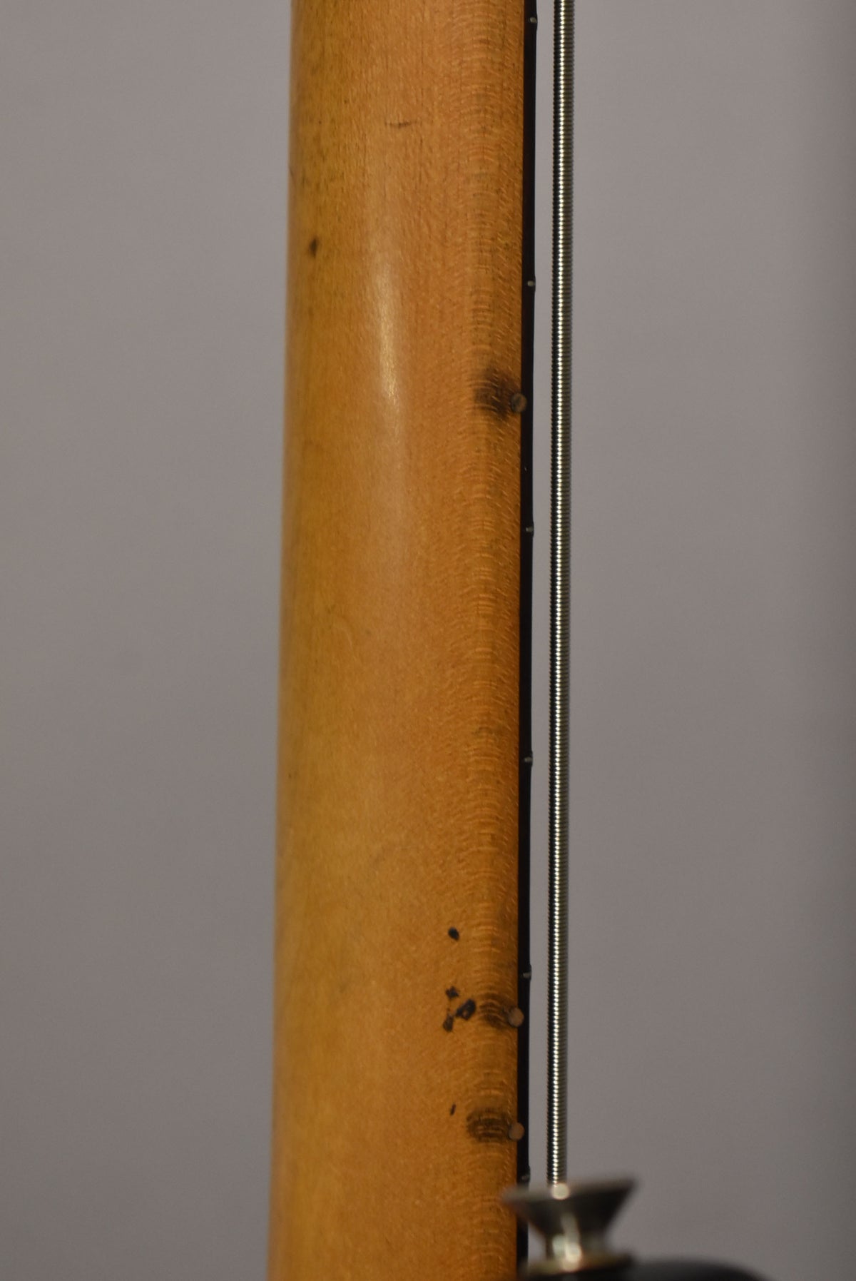 Close-up of the bass neck's back, showing a worn, light brown finish with dark spots and visible wood grain.