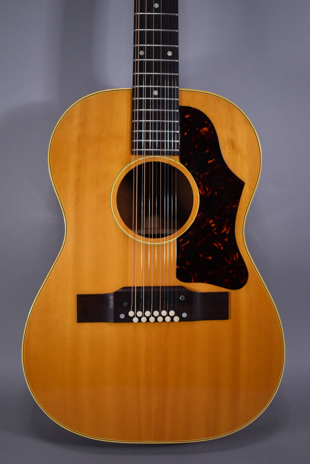 Full-frame view of a natural finish 12-string acoustic guitar with a dark tortoiseshell pickguard and white bridge pins.