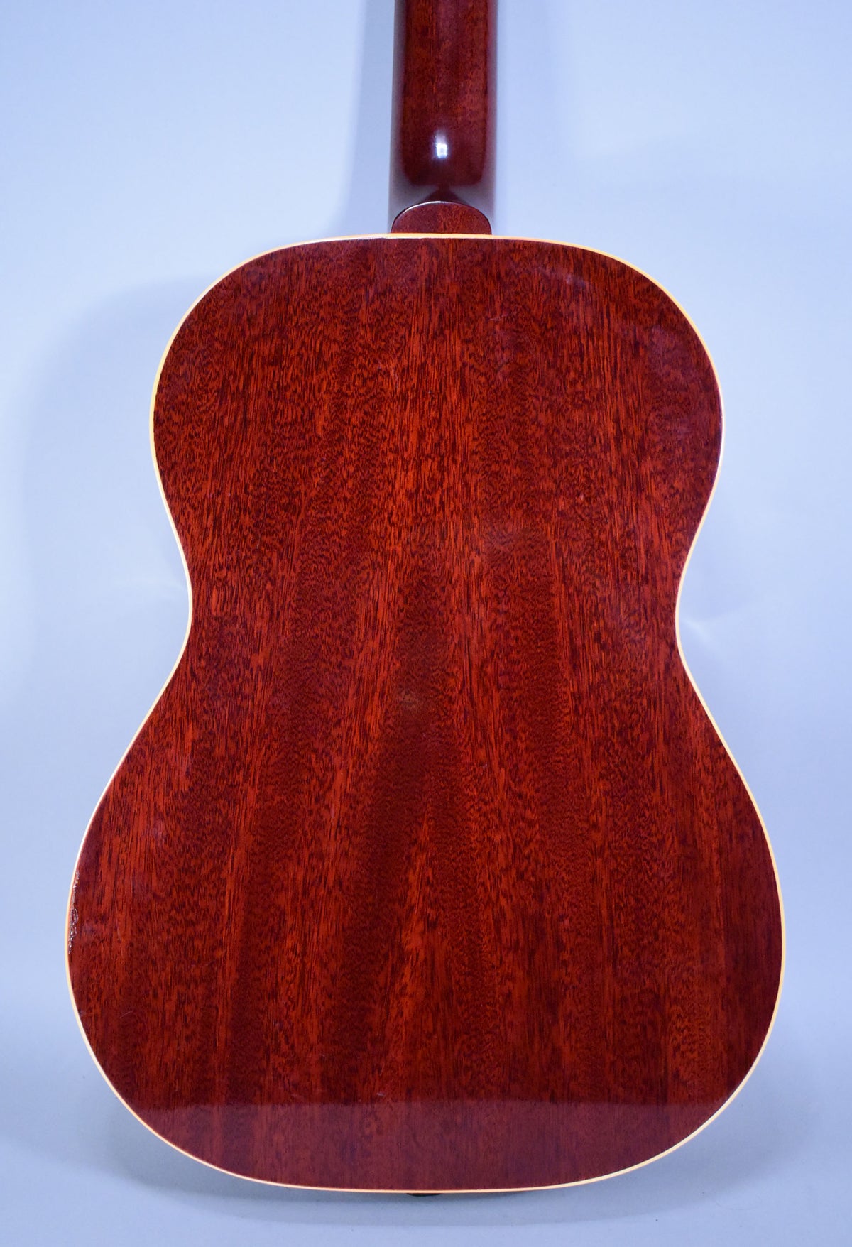 The full back of the acoustic guitar is visible, showing a reddish-brown wood grain with light binding and a glossy finish.