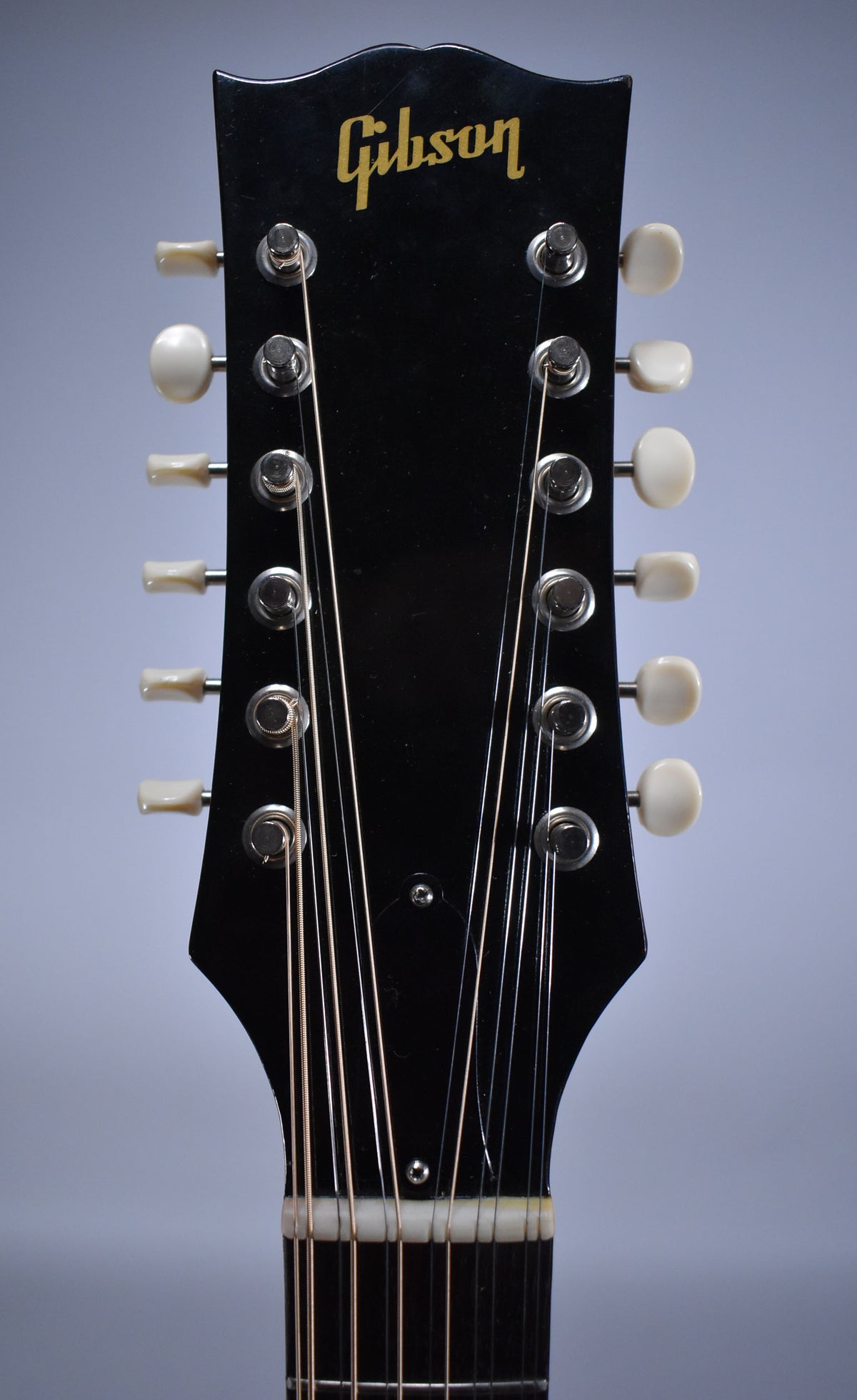 Close-up of the guitar's glossy black headstock with gold lettering, showing 12 tuning pegs with cream buttons and strings.