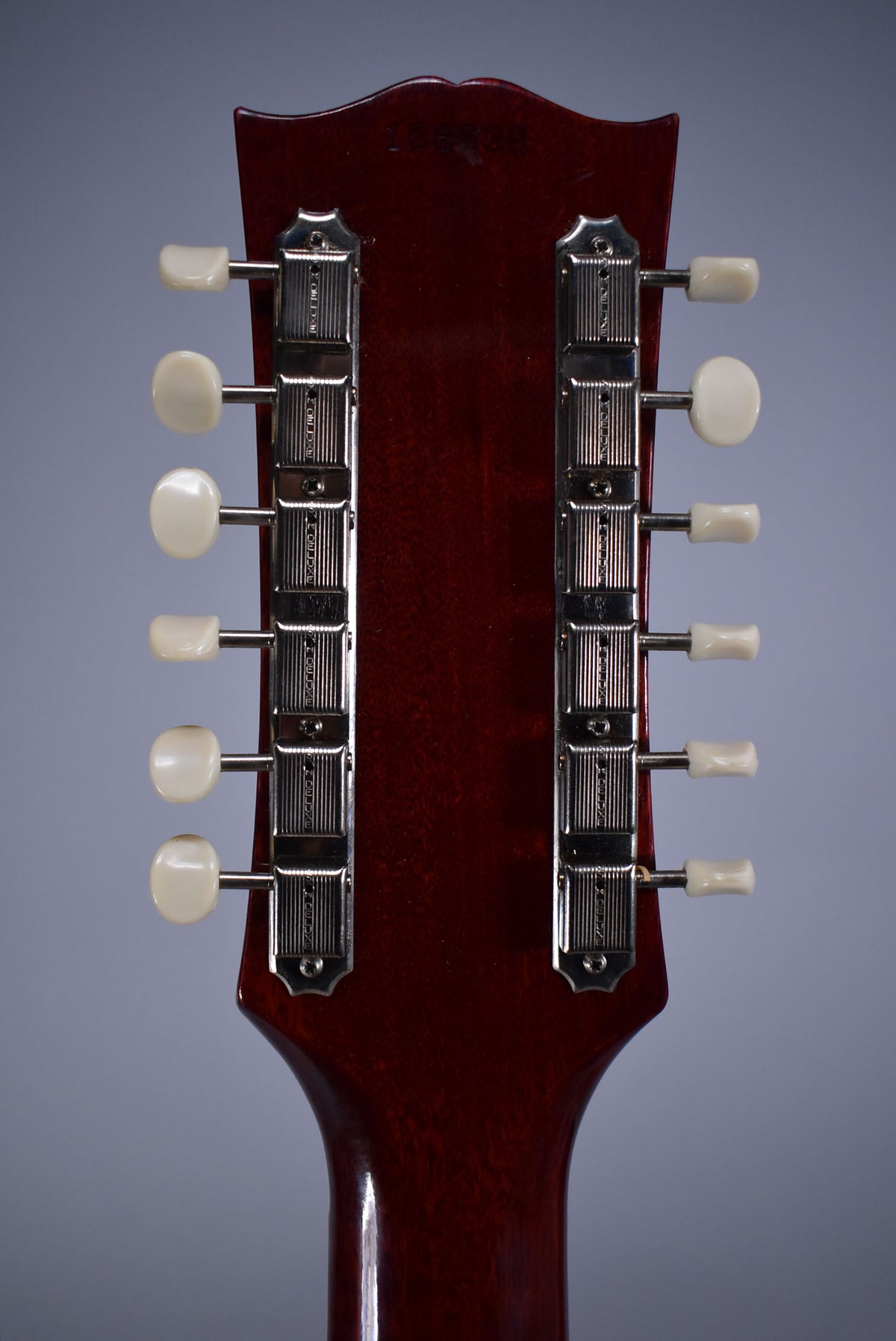 The back of a dark cherry-stained headstock with a glossy finish, showing two rows of six chrome tuners with cream buttons.