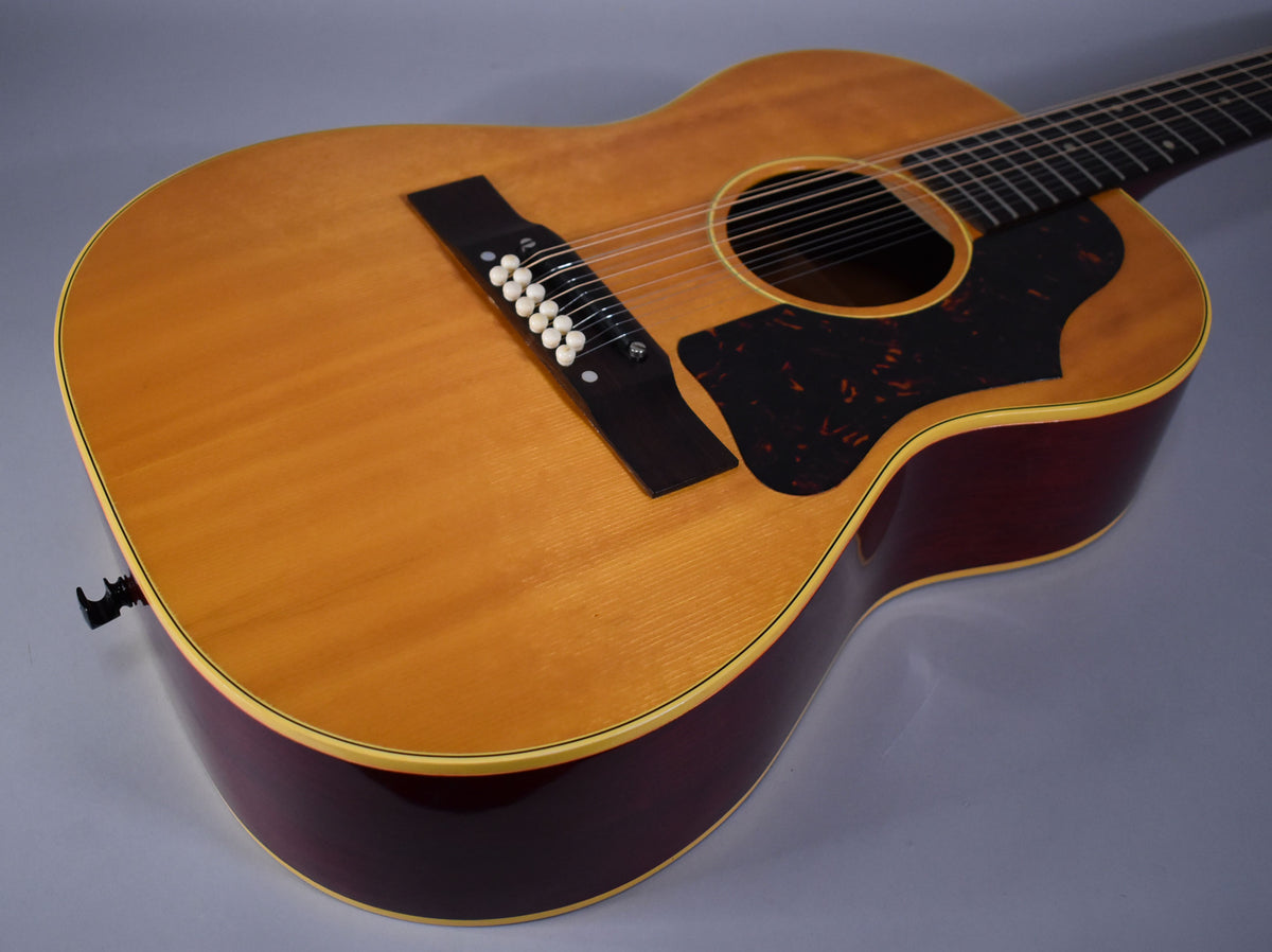 The guitar's natural finish top shows light wood grain, with a dark tortoiseshell pickguard and a dark red body.