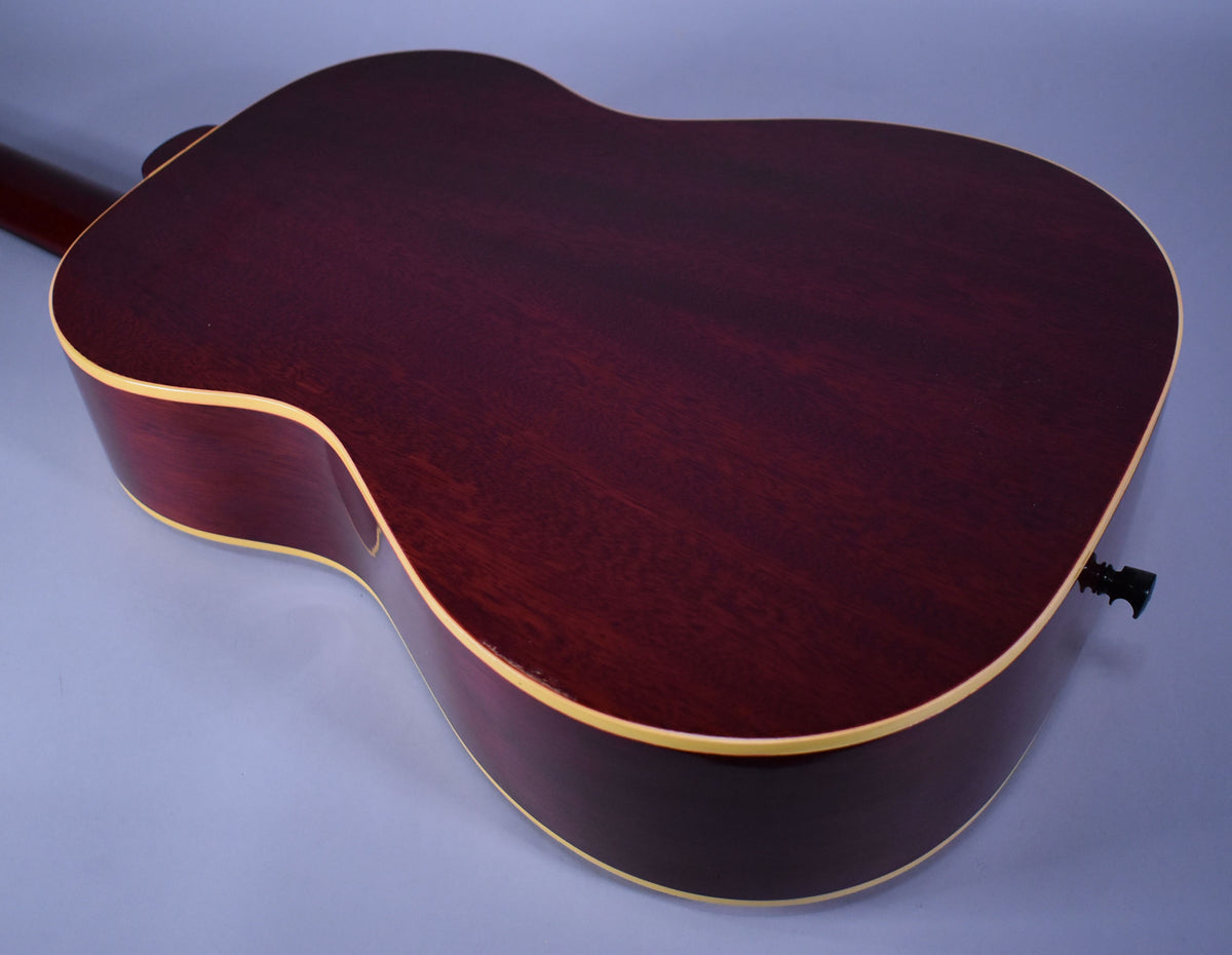 The back of a dark red acoustic guitar with a natural finish, showing light binding and a black endpin jack.