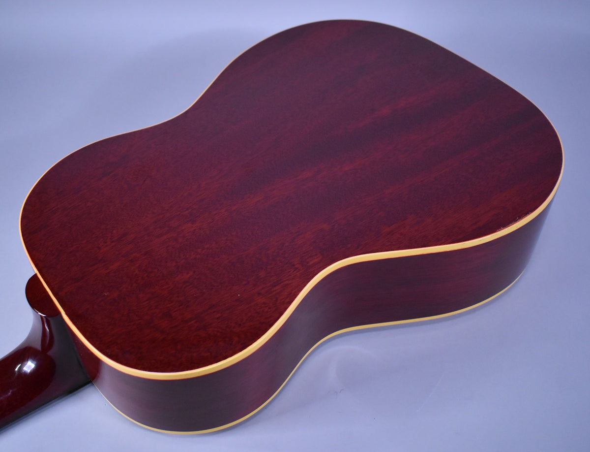 The guitar's dark reddish-brown back and sides are visible, with light binding around the edges and some finish checking.