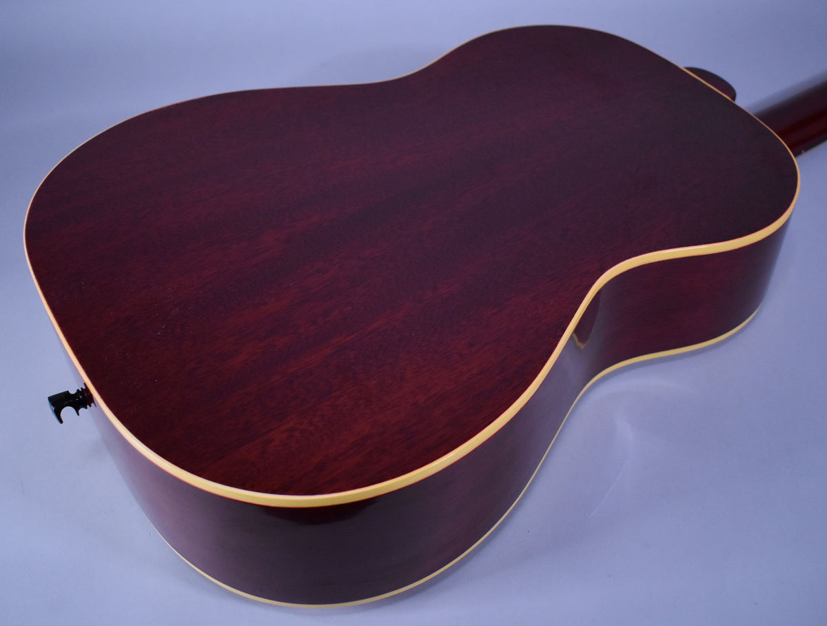 The guitar's dark red-brown back and sides are visible from above, with light binding and a black endpin jack.