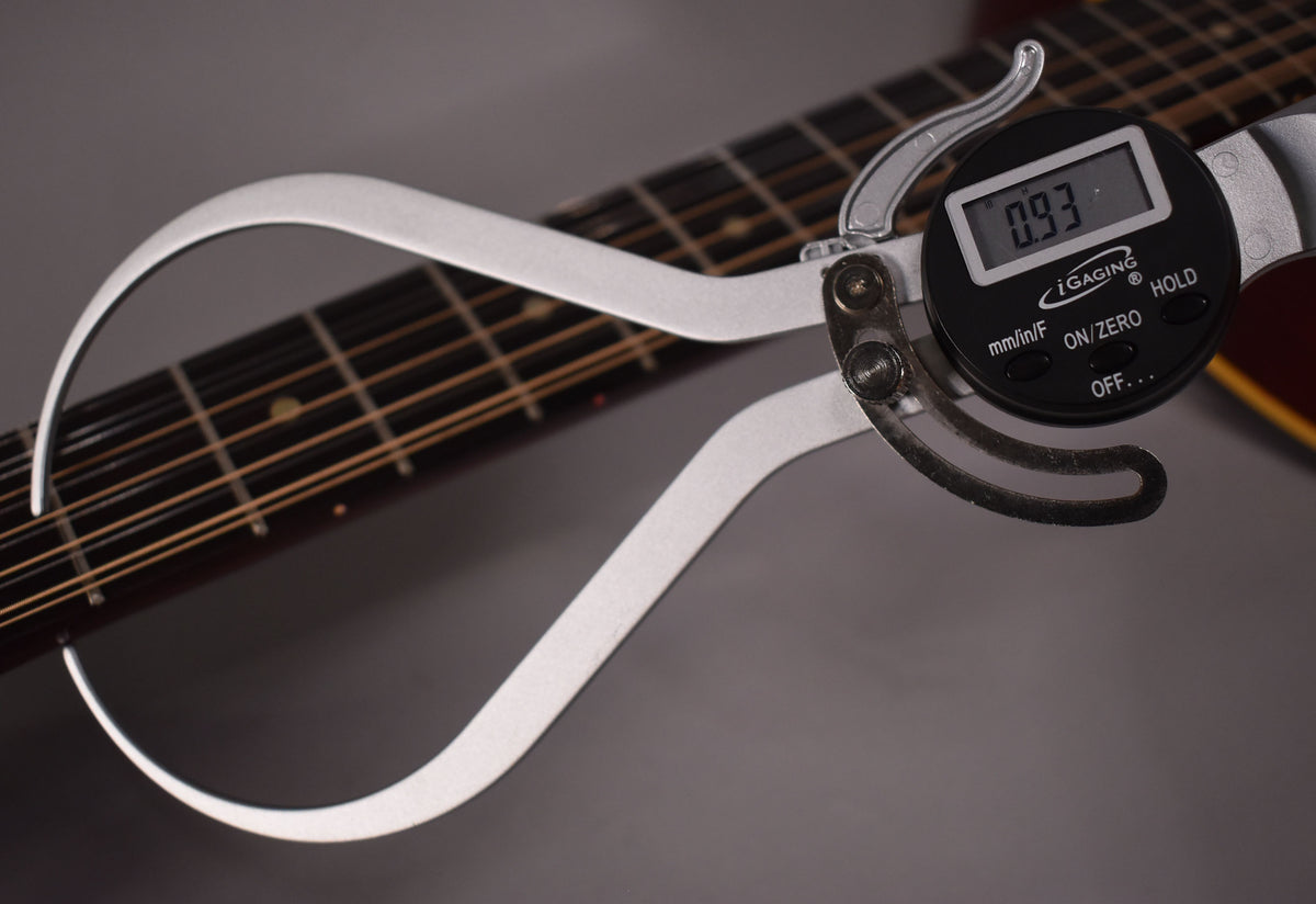 A digital caliper measures the natural finish 12-string guitar's neck, showing a reading of 0.93 inches.