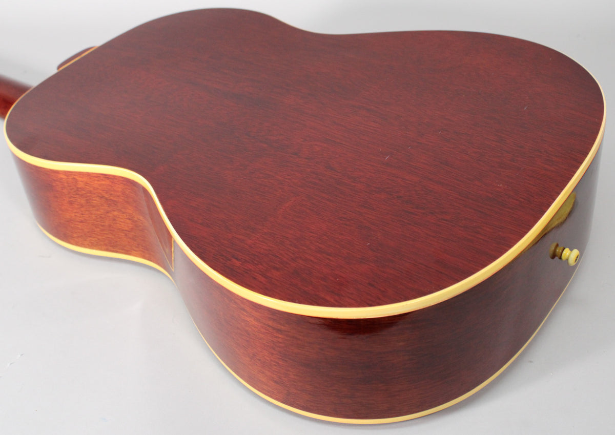 The guitar's dark reddish-brown back and sides are visible, with cream binding and light wear, angled from the lower bout.